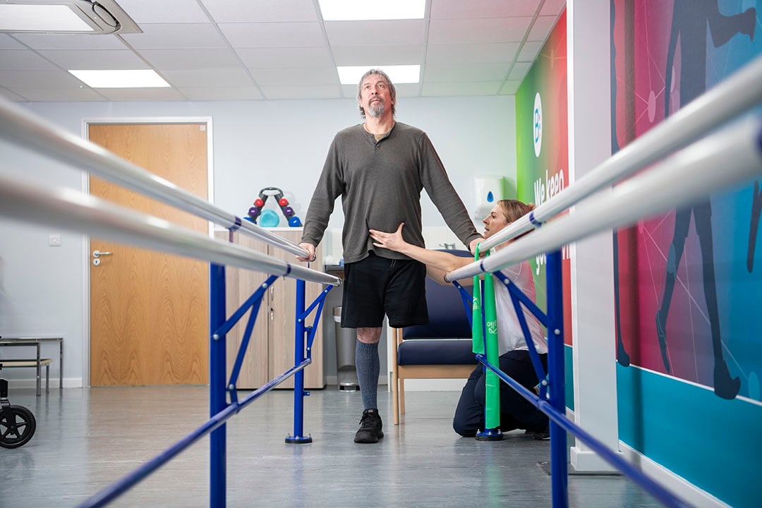 Physio helping a patient to stand at the parallel bars